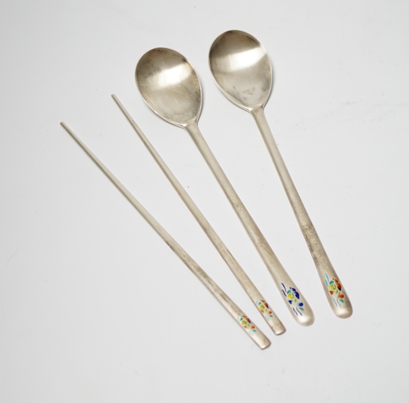 A Korean 990 standard white metal pair of chopsticks, 20cm and two matching spoons with enamelled decoration.